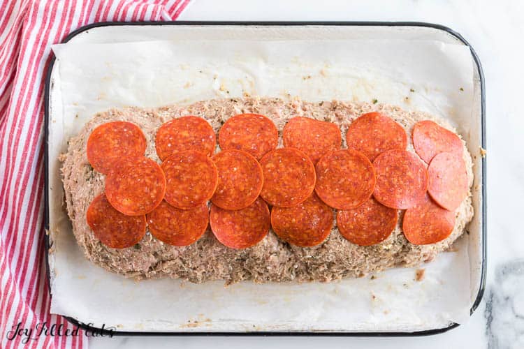 uncooked meatloaf in a shallow baking dish topped with pepperoni slices