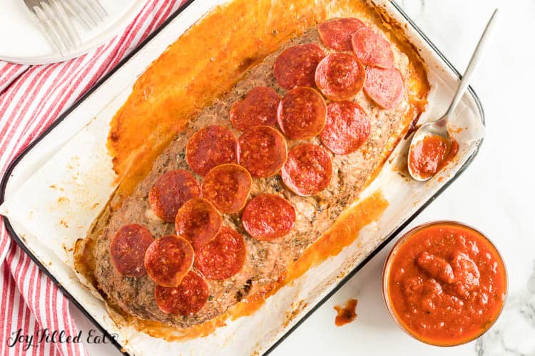 uncut meatloaf in a shallow baking dish next to a bowl of marinara sauce. top of meatloaf is covered in pepperoni slices