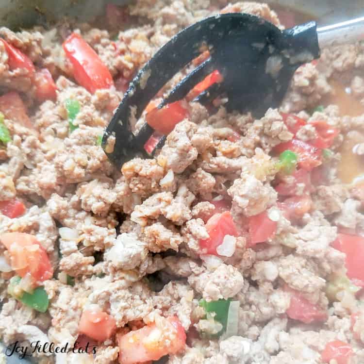Close up on ground meat and vegetable mixture being cooked in a skillet with cooking utensil