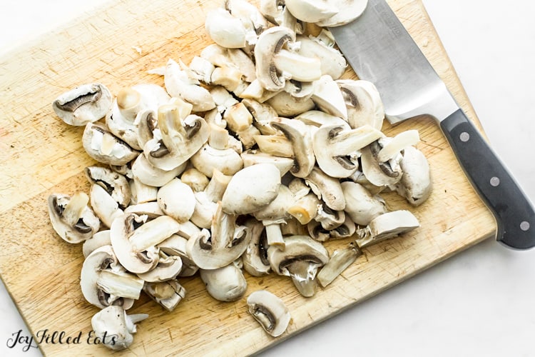 large wooden cutting board of sliced mushrooms with a chef's knife