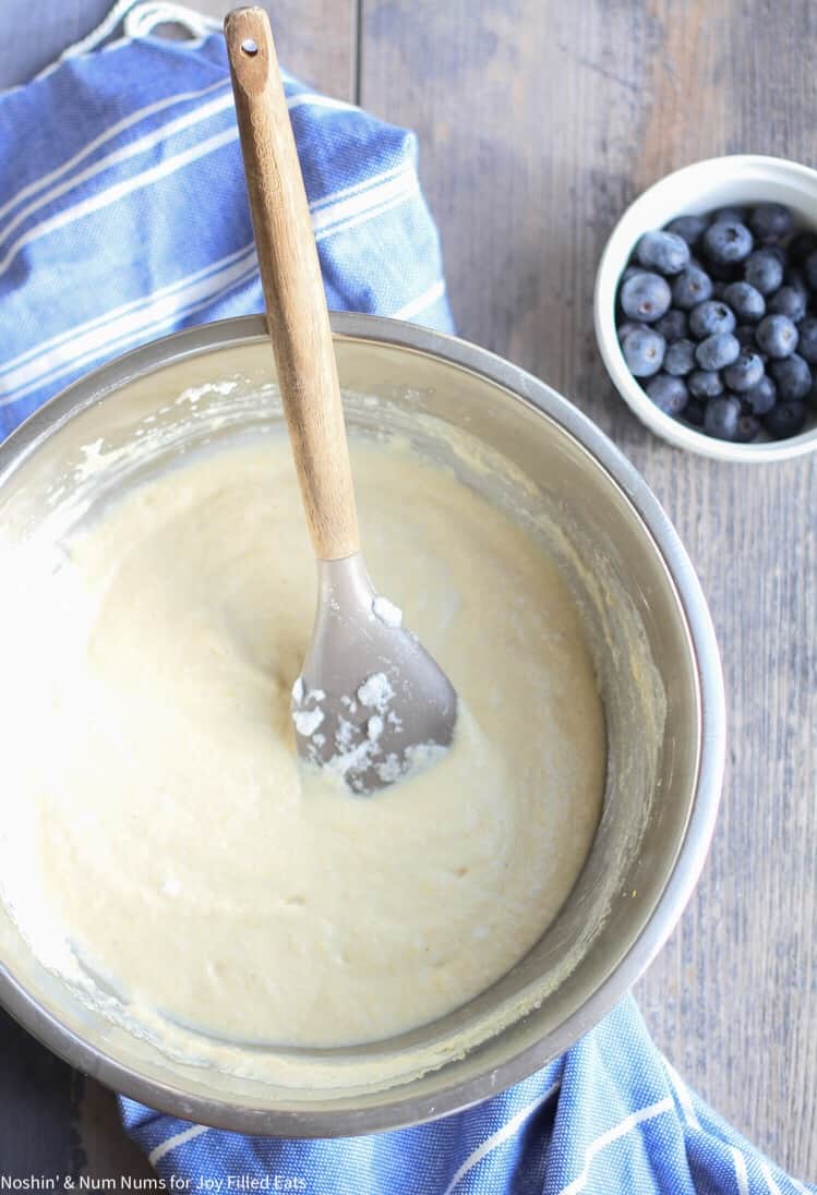 pancake batter in a large mixing bowl with mixing spoon next to a smaller bowl of blueberries
