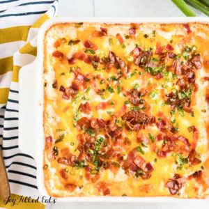 overhead view of white casserole dish filled with loaded cauliflower casserole, topped with bacon pieces and chives