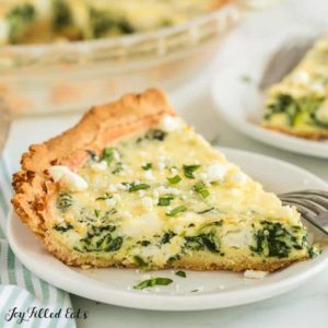 spinach and feta quiche slice on white plate with fork resting on plate