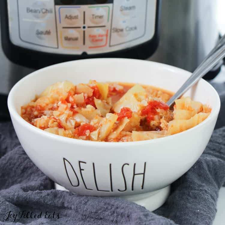 cabbage roll soup and spoon in a white soup bowl that read "Delish" in front of an instant pot