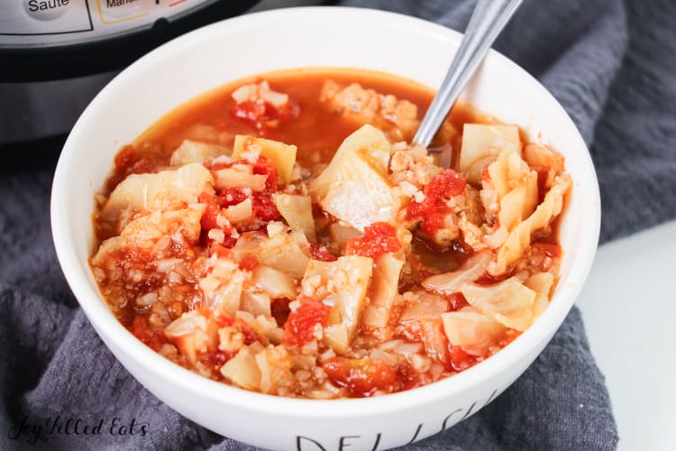 cabbage roll soup in white soup bowl with spoon on a black, cloth napkin