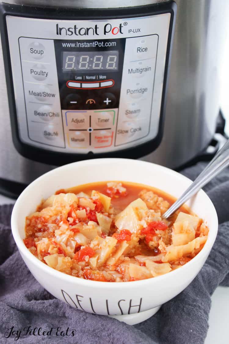 cabbage roll soup in white bowl with spoon in front of instant pot all placed on a cloth napkin