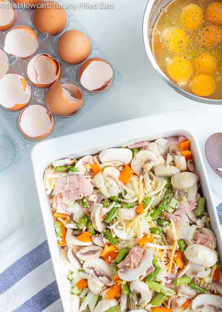 overhead view of casserole dish filled with chopped vegetables next to carton of cracked egg shells and a mixing bowl filled of cracked eggs