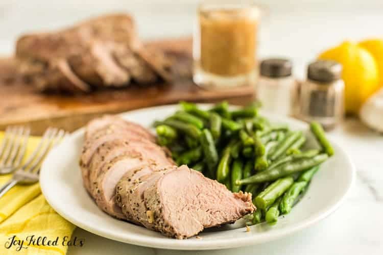 Slow cooked pork tenderloin slices fanned out on a plate with a serving of green beans