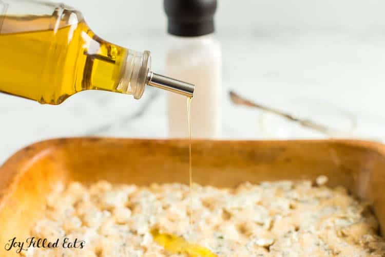 olive oil being drizzled onto bread dough in baking dish