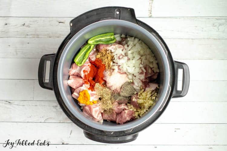 overhead view of instant pot filled with raw pork shoulder, jalapenos, and other ingredients 