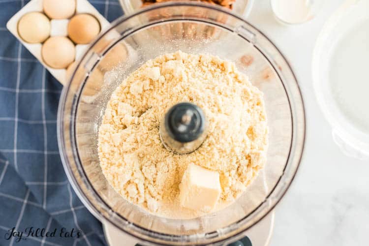 overhead view of food processor with ingredients for pie crust, next to carton of eggs