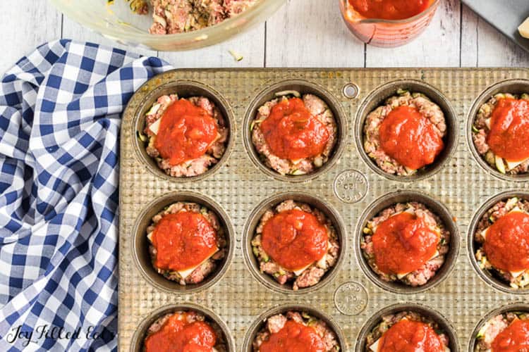 overhead view of mini muffin tin filled with tiny meatloaves topped with sauce before cooking