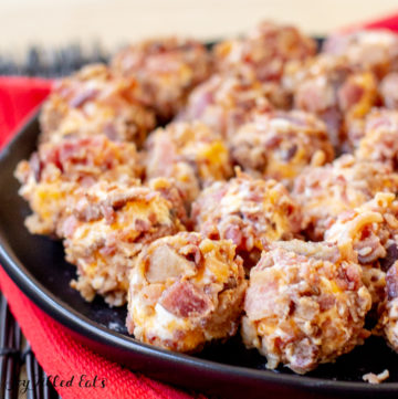 Bacon Cheddar Mini Cheese Balls on a black plate on top of a red towel and black bamboo placemat