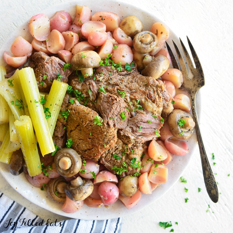 Large serving Plate of instant pot beef roast with celery, radishes and mushrooms. Large serving fork on plate.