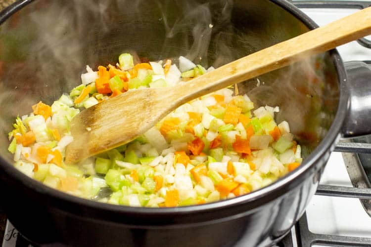 Pot and wooden spoon on stove top filled with onions carrots and celery