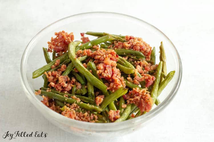 Oven roasted green beans and crumbled bacon mixed together in glass bowl