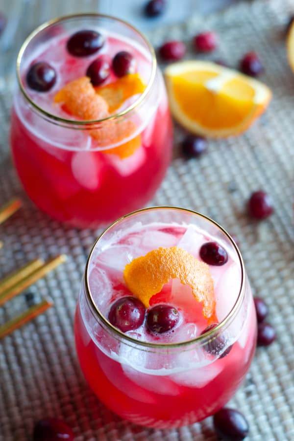 overhead view of two glasses of vodka cranberry spritzer surrounded by whole cranberries and orange wedges