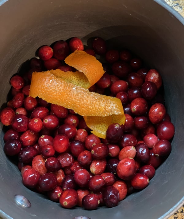 overhead view of saucepan with whole cranberries and spiraled orange peel