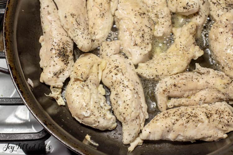 pan filled with seasoned chicken tenders on stove top