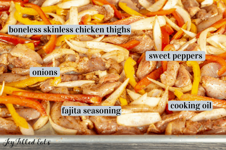 Sheet pan of ingredients including boneless, skinless chicken thighs, onions, sweet peppers, fajita seasoning, cooking oil