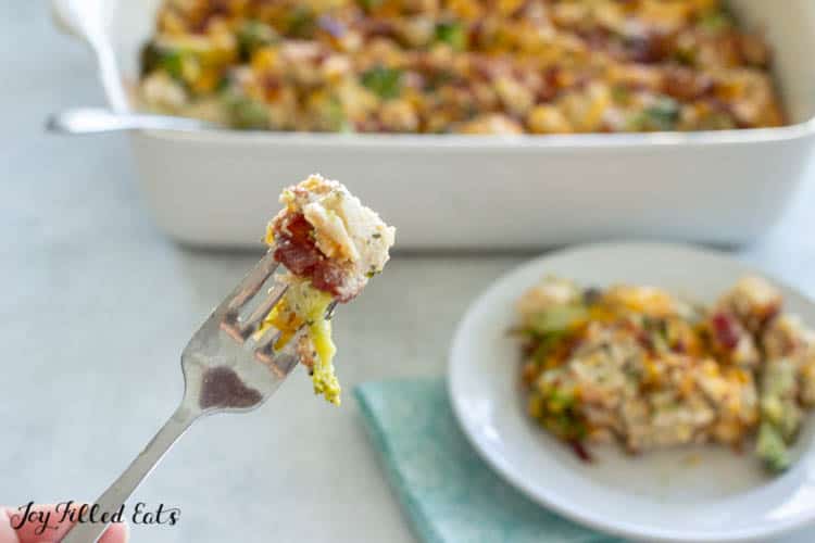 Fork with bite of chicken bacon ranch casserole in front of plate and casserole dish of meal