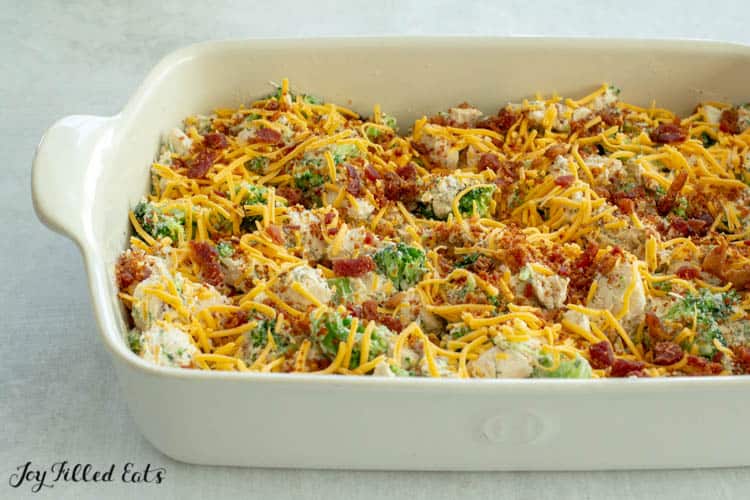White casserole dish of Chicken Bacon Ranch Casserole sprinkled with shredded cheese