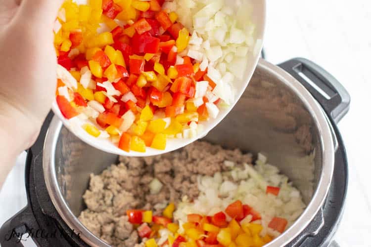 Hand pouring bowl of diced peppers and onions into instant pot