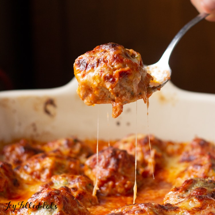 Spoon of cheesy Meatball from Meatball casserole dish below