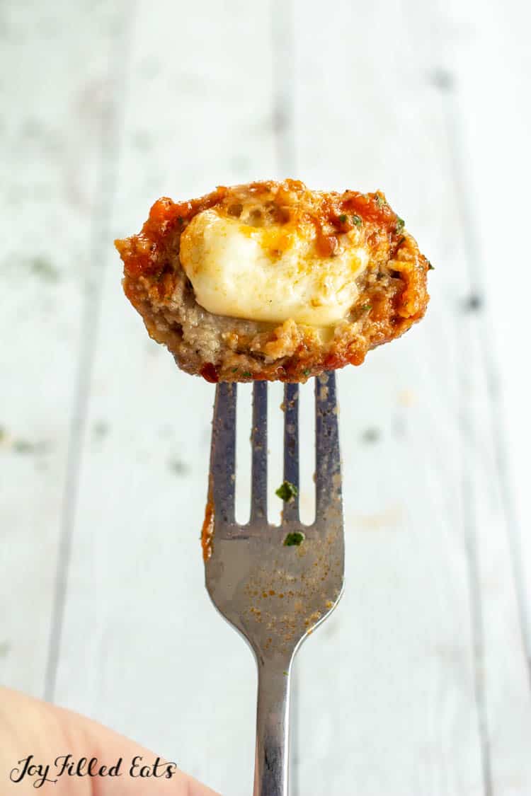 Fork holding half of mozzarella stuffed meatball to show melted cheese