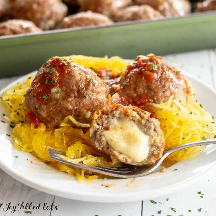 Plate of spaghetti squash with mozzarella stuffed meatballs and fork. One meatball is sliced open to see melted cheese