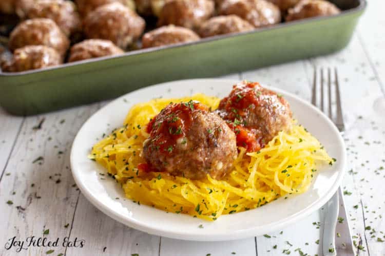 Plate of spaghetti squash with mozzarella stuffed meatballs. Next to baking dish of more meatballs