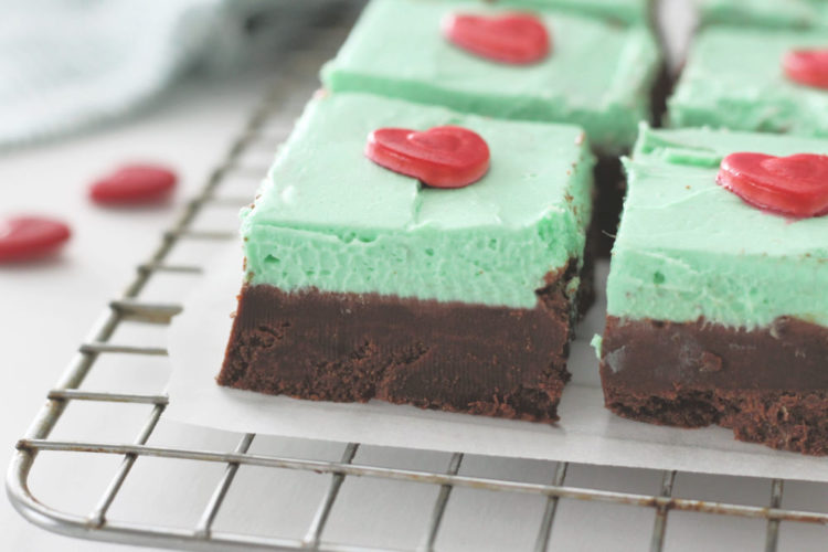 Close up of two layer mint chocolate fudge on a cooling rack. Top mint green fudge layers are topped with red candy heart