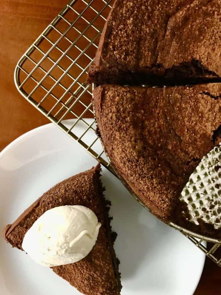 close up overhead view of almond flour cake on cooling rack with slice cut out. Slice of cake next to cooling rack on separate plate with scoop of ice cream