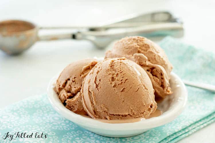 Small dish of low carb chocolate ice cream scoops on a decorative blue napkin. Metal ice cream scoop in background