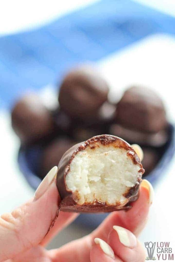 Hand holding chocolate covered buttercream candy with bite missing in front of bowl of similar candies