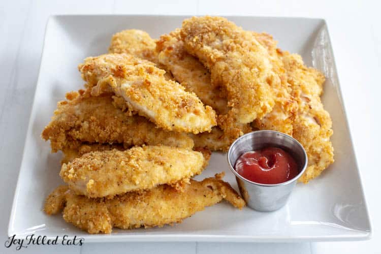 White platter with healthy baked chicken tenders with a small container of ketchup