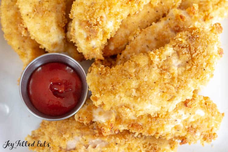 close up of platter with healthy baked chicken tenders with a small container of ketchup