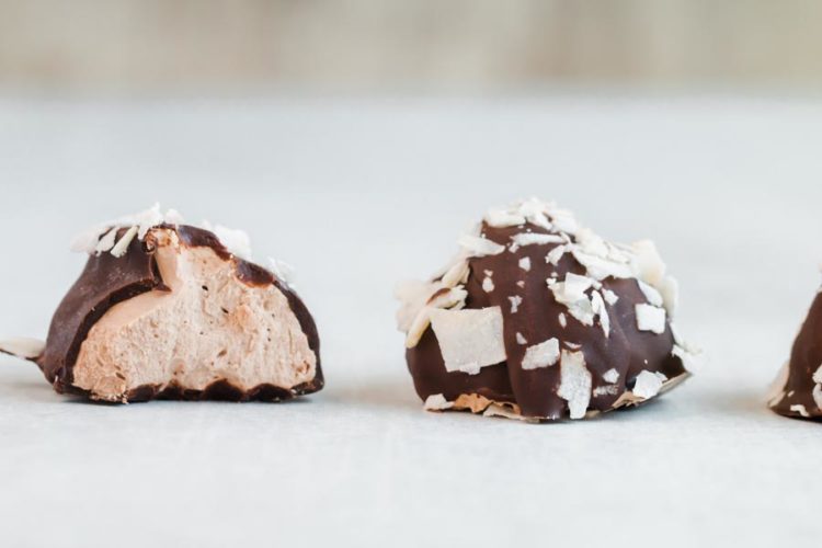 close up of keto almond joy cream truffles with one truffles sliced in half, filling side to the camera