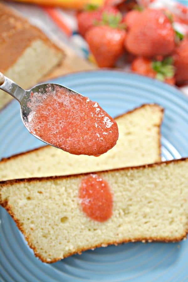 Spoonful of strawberry jam drizzling onto strawberry pound cake slices on blue plate