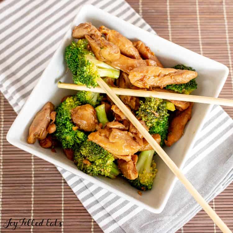 Keto Teriyaki Chicken with broccoli and chop sticks in square bowl on gray and white striped napkin