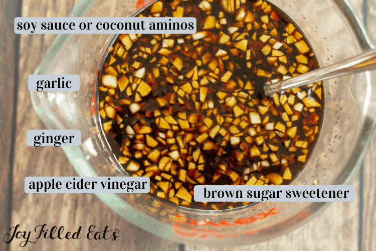 overhead view of ingredients in measuring cup with spoon include soy sauce or coconut aminos, garlic, ginger. apple cider vinegar and brown sugar sweetener