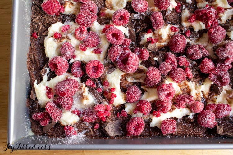 Dark chocolate cheesecake brownies batter in a baking dish topped with frozen raspberries