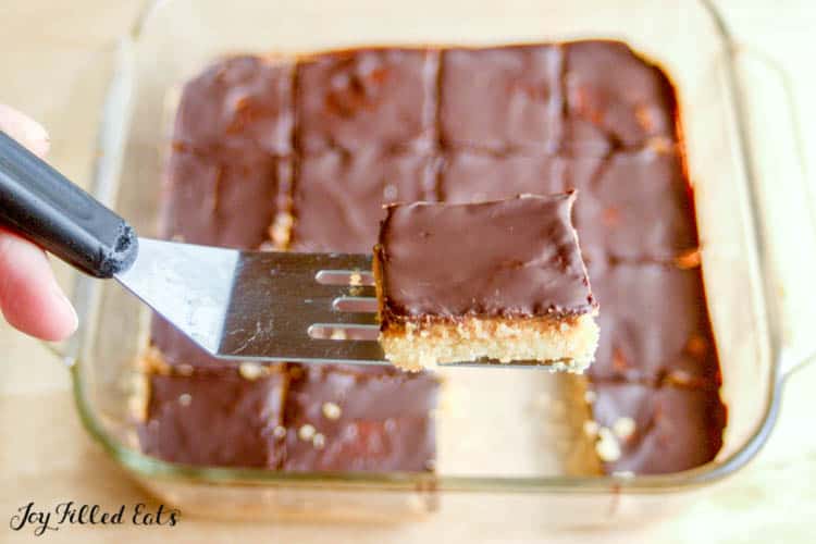 Serving spatula with slice of homemade tagalong bars in front of baking dish of bars