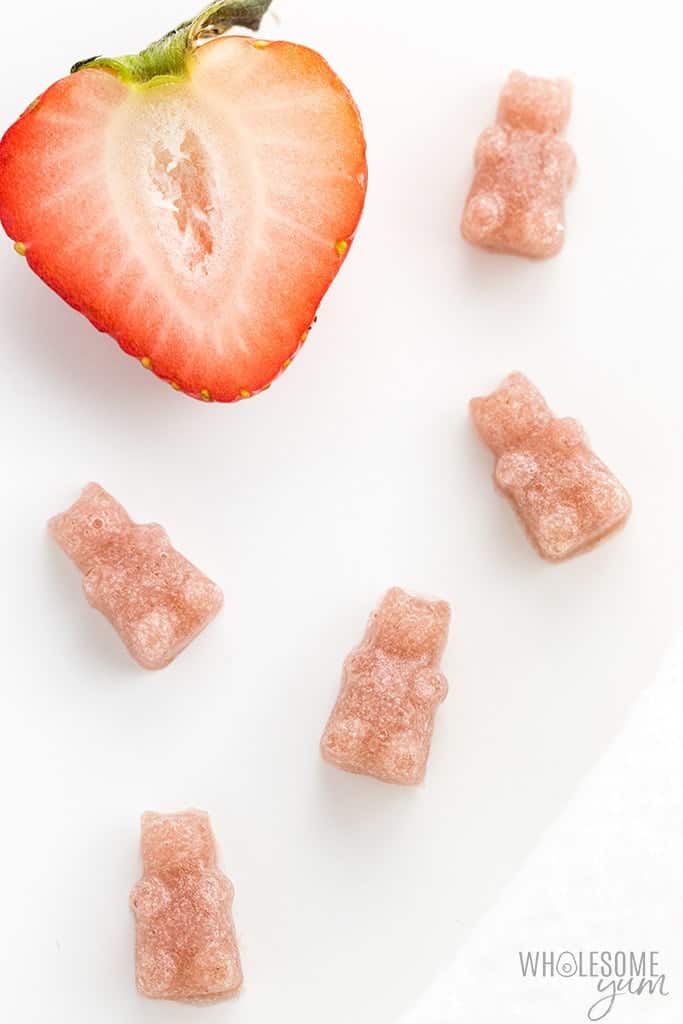 close up of five homemade sugar free gummy bears with half a sliced strawberry