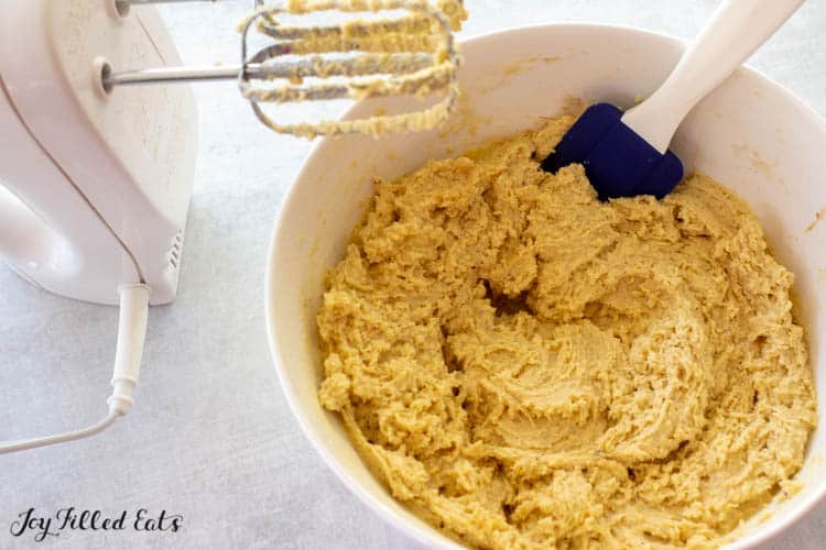 White mixing bowl of almond flour banana muffin batter with used hand mixer and spatula