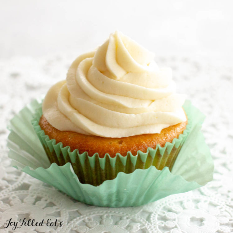 Almond Flour Cupcake topped with buttercream frosting in a light blue cupcake wrapper pulled away from the cupcake. Sitting on a decorative table cloth