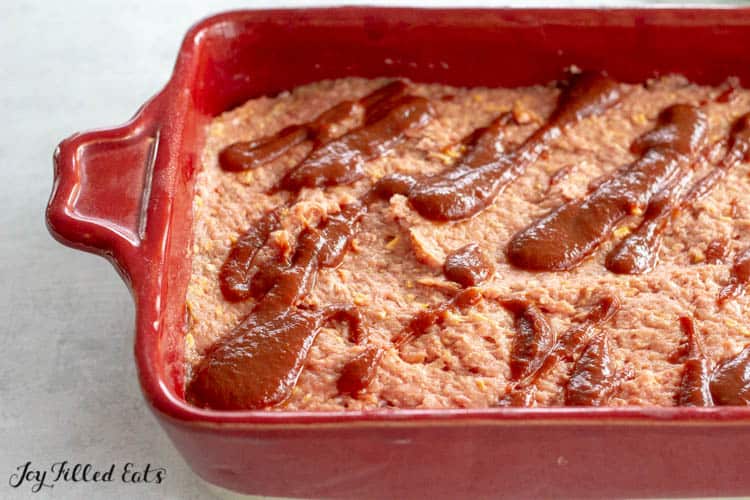 bbq meatloaf formed into red casserole dish with bbq sauce spooned onto mixture prior to cooking