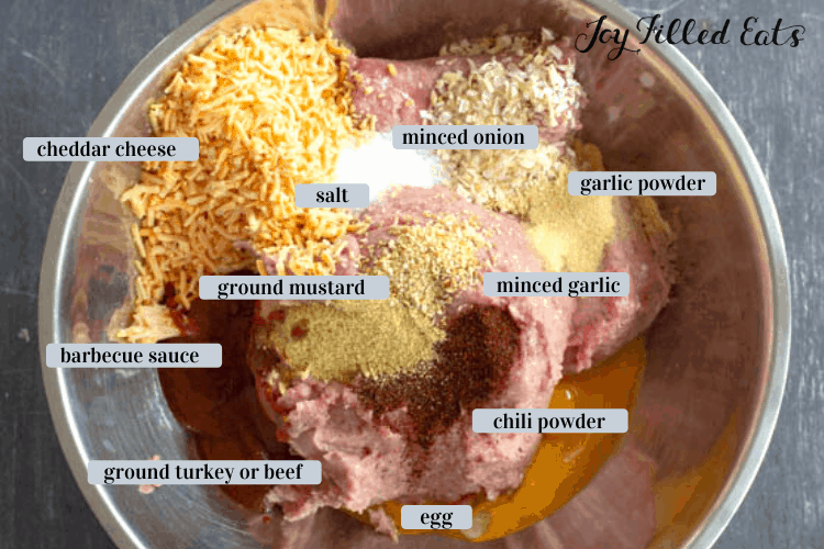 Overhead shot of mixing bowl with ingredients including ground beef or turkey, egg, chili powder, minced garlic, garlic powder, minced onion, salt, ground mustard, cheddar cheese