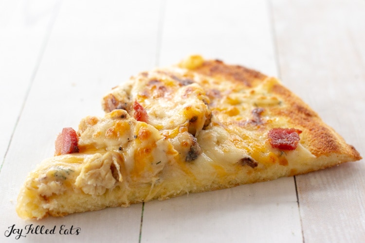 Slice of coconut flour pizza crust topped with cheese, bacon and chicken pieces