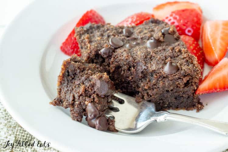 low carb brownie on a plate with small bite broken off on fork. Plate also includes a side of cut strawberries
